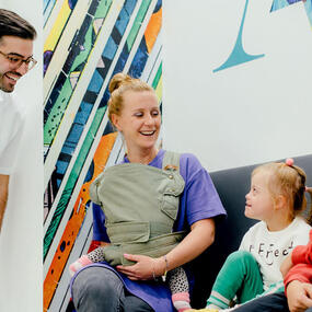 Eine Familie sitzt lachend im Wartezimmer einer modernen Kinderzahnarztpraxis.