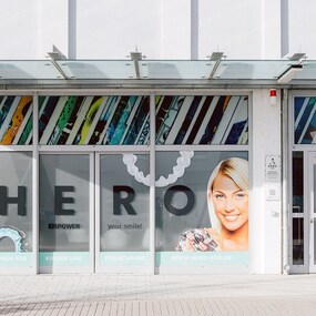 Praxisfassade einer Kieferorthopädie mit lächelnden Patienten und modernem Logo-Design.